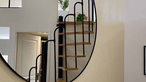 Un miroir rond reflétant un escalier avec des marches en bois et des rampes en métal noir.