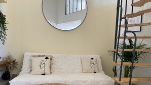 Un salon moderne avec un canapé, deux petites tables rondes en bois, un miroir rond et une étagère en bois en forme d’échelle.