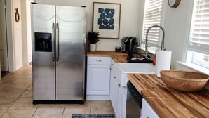 A modern kitchen with a stainless steel refrigerator, white cabinetry, a wooden countertop, a sink, and a window with blinds. - Beautiful Forsyth Park Victorian - Walk to it all! (Savannah)