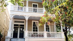 A two-story house with a front porch, a brick foundation, and a white railing. - Beautiful Forsyth Park Victorian - Walk to it all! (Savannah)