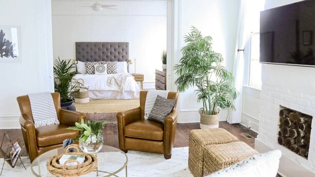 A modern living room with a large bed, leather armchairs, a glass coffee table, and a fireplace.