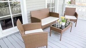 A wicker outdoor seating area with a table and chairs, a glass-top coffee table, and a decorative vase with flowers.