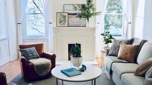 Un salón acogedor con chimenea, un sillón de cuero marrón, un sofá blanco y una mesa de centro redonda con un libro.