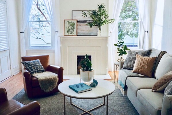 Un salon chaleureux avec une cheminée, un fauteuil en cuir marron, un canapé blanc et une table basse ronde sur laquelle repose un livre.