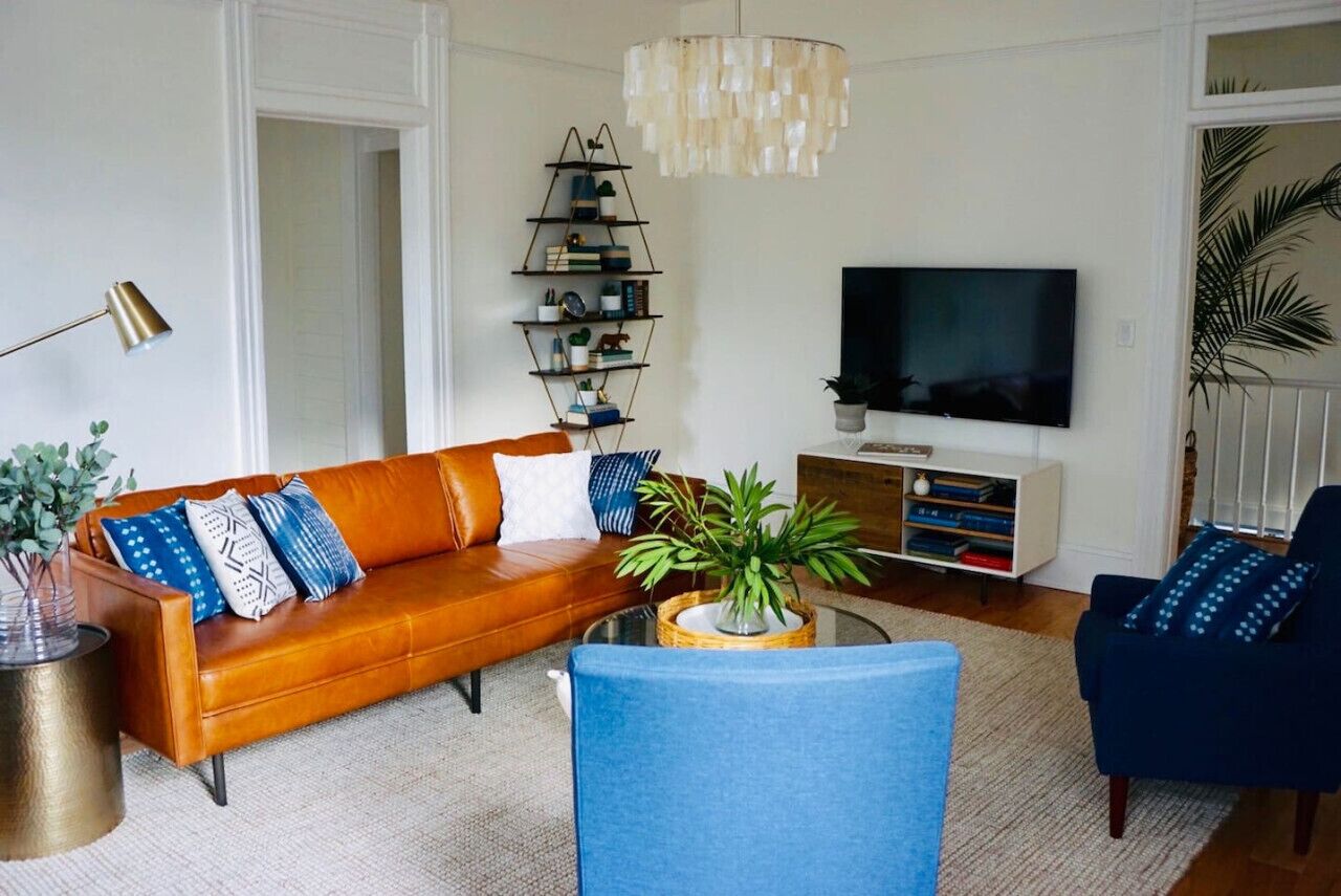 A modern living room with a brown leather sofa, a blue armchair, a coffee table with a plant, a bookshelf, and a flat-screen TV.