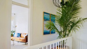Una escalera con barandilla blanca que lleva a una habitación con una planta grande en maceta y un cuadro de una playa.