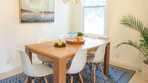 A dining area with a wooden table, white chairs, a chandelier, a painting, and a window with a view. - Beautiful Forsyth Park Charmer - Amazing Location! (Savannah)
