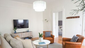 A living room with a sofa, two armchairs, a coffee table, a television, and a chandelier. - Beautiful Forsyth Park Charmer - Amazing Location! (Savannah)