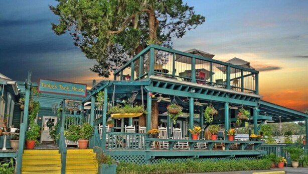 A two-story building with a sign reading "Tubby's Tank House." It features outdoor seating with potted plants and a staircase leading to the entrance.