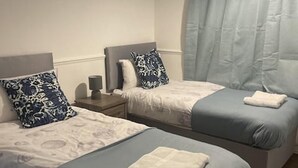A hotel room with two single beds, each with a pillow and a blanket. There is a nightstand with a lamp between the beds. - Tms 3bdr Tilbury - Free Parking (Tilbury)