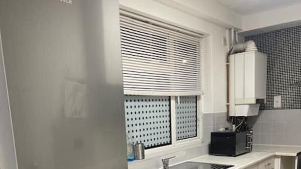 A compact kitchen with a Bosch refrigerator, a built-in washing machine, a sink, and a window with blinds. - Tms 3bdr Tilbury - Free Parking (Tilbury)