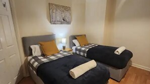 A hotel room with two beds, each with a checkered blanket and a pillow. There is a painting on the wall above the beds. - Remarkable 3-bed House in Tilbury (Tilbury)