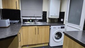 A compact kitchen with a washing machine, a sink, and wooden cabinets. - Remarkable 3-bed House in Tilbury (Tilbury)