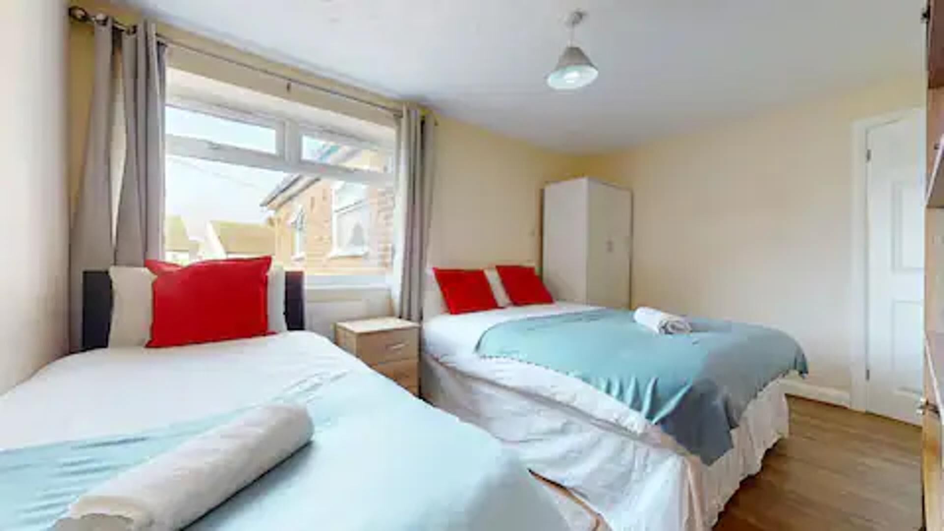 A hotel room with two beds, a wardrobe, and a window with curtains.