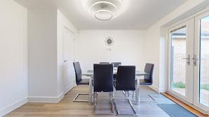 Een moderne eetruimte met een glazen tafel, zwarte stoelen en een plafondlamp.