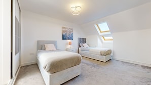 Een moderne slaapkamer met twee bedden, een dakraam, een nachtkastje en een wandlamp.