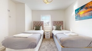 A modern bedroom with two beds, a nightstand, a window, and a painting.