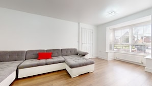 Een moderne woonkamer met een grijze modulaire bank, een rode kussen en een groot raam met zonwering.