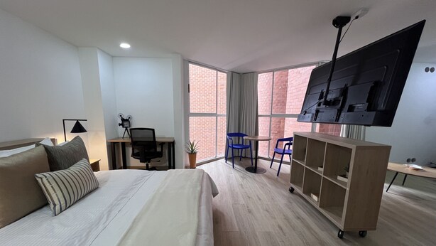 Quarto de hotel moderno com cama, escrivaninha, cadeira, TV e vista para o exterior.
