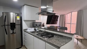 Uma cozinha moderna com geladeira de aço inoxidável, micro-ondas embutido, fogão a gás e uma janela grande com cortinas.