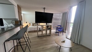 Quarto de hotel moderno com cama, televisão, pequena mesa de jantar e área de estar com cadeiras.