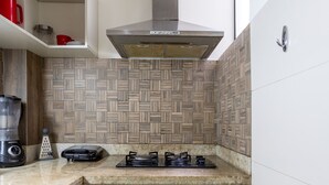 Una cocina compacta con estufa a gas, extractor de humos integrado y encimera con licuadora y rallador.
