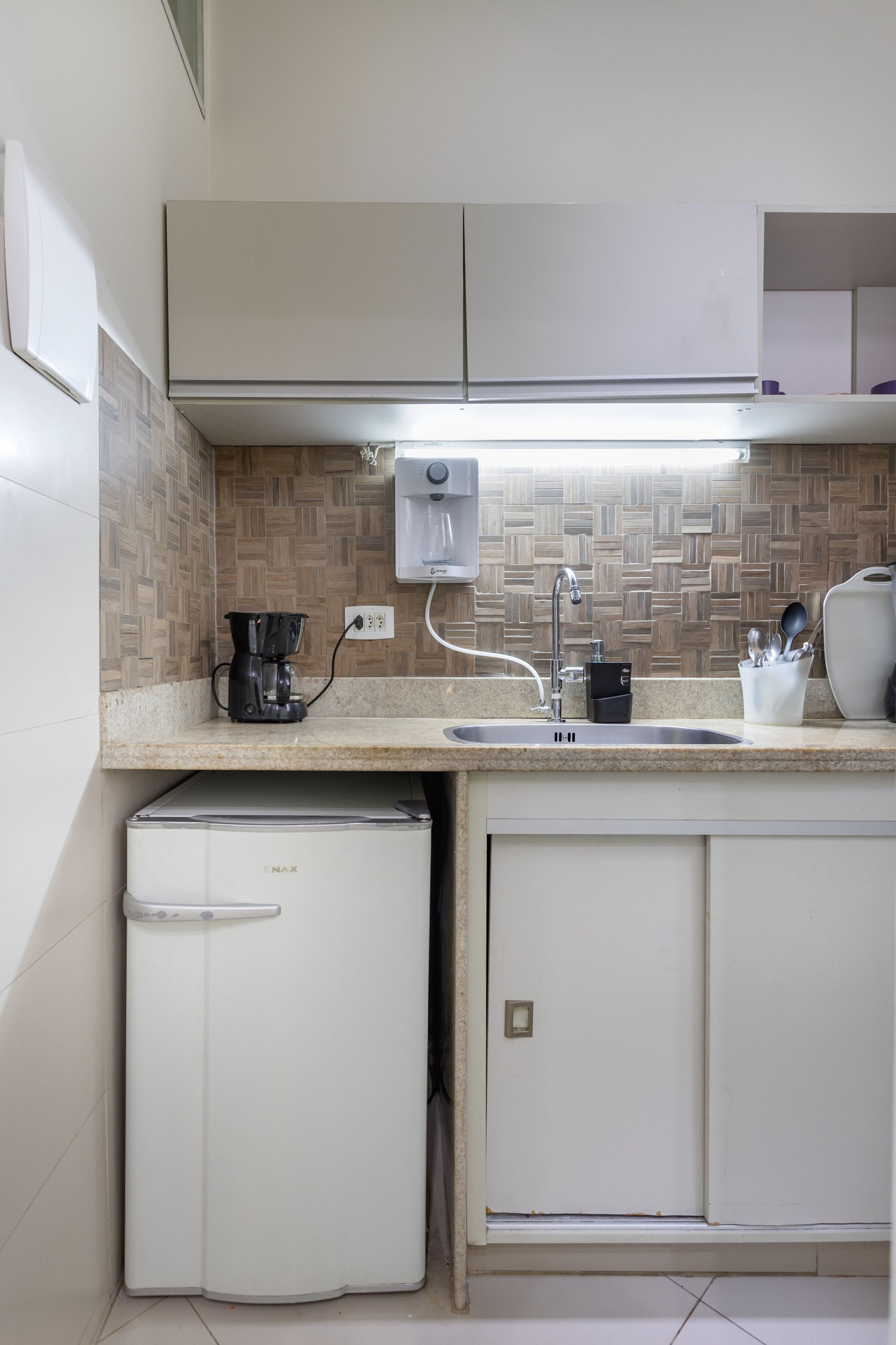 A compact kitchenette with a built-in refrigerator, a coffee maker, a sink, and a utensil holder.