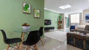 Una sala de estar moderna con una mesa de comedor de vidrio, sillas negras, un sofá y un televisor.