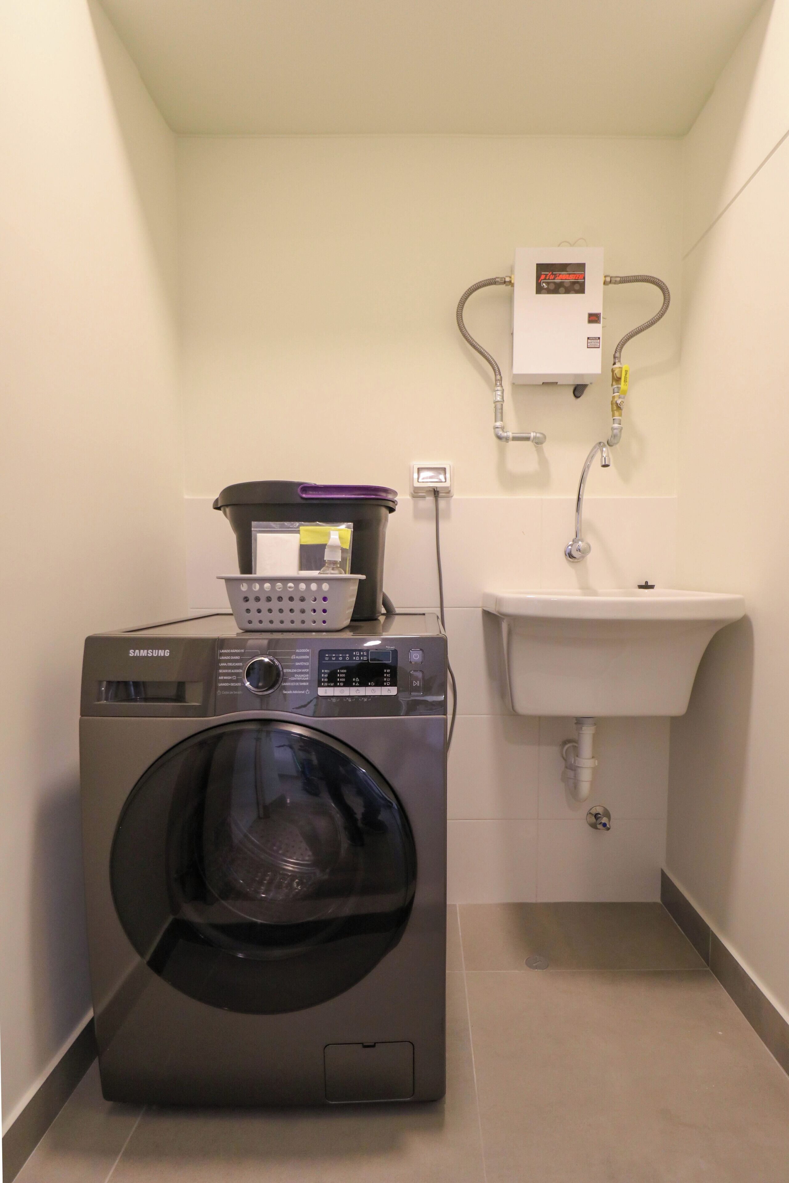 A compact laundry room with a Samsung washer, a sink, and a water heater.