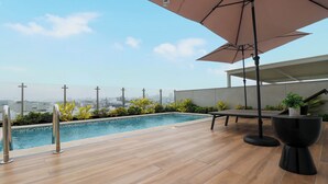 A rooftop pool area with a view of the city skyline, a wooden deck, and a seating area with an umbrella. - Pod by Wynwood House (Lima)
