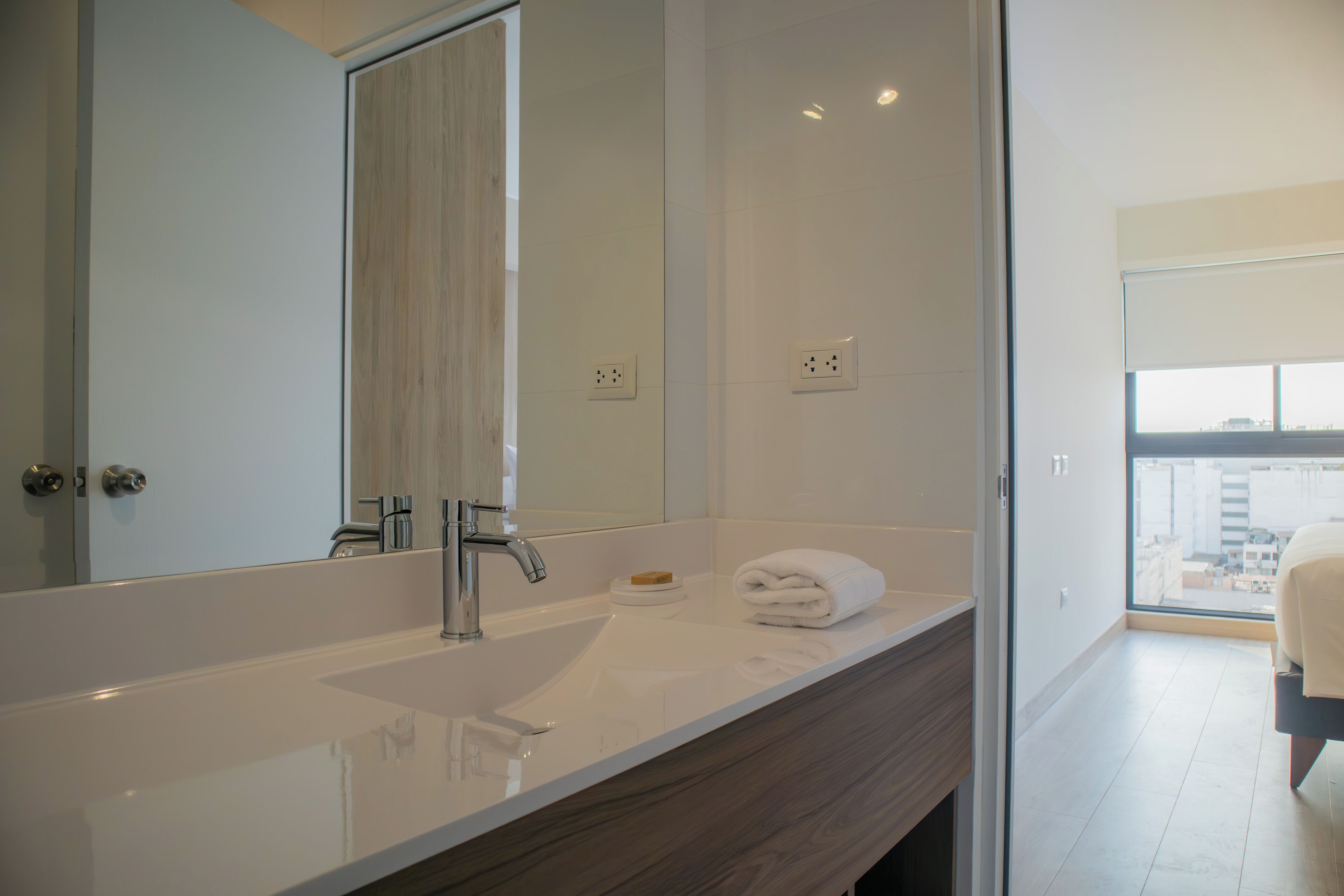 A modern bathroom with a large mirror, a white sink, and a wooden vanity.