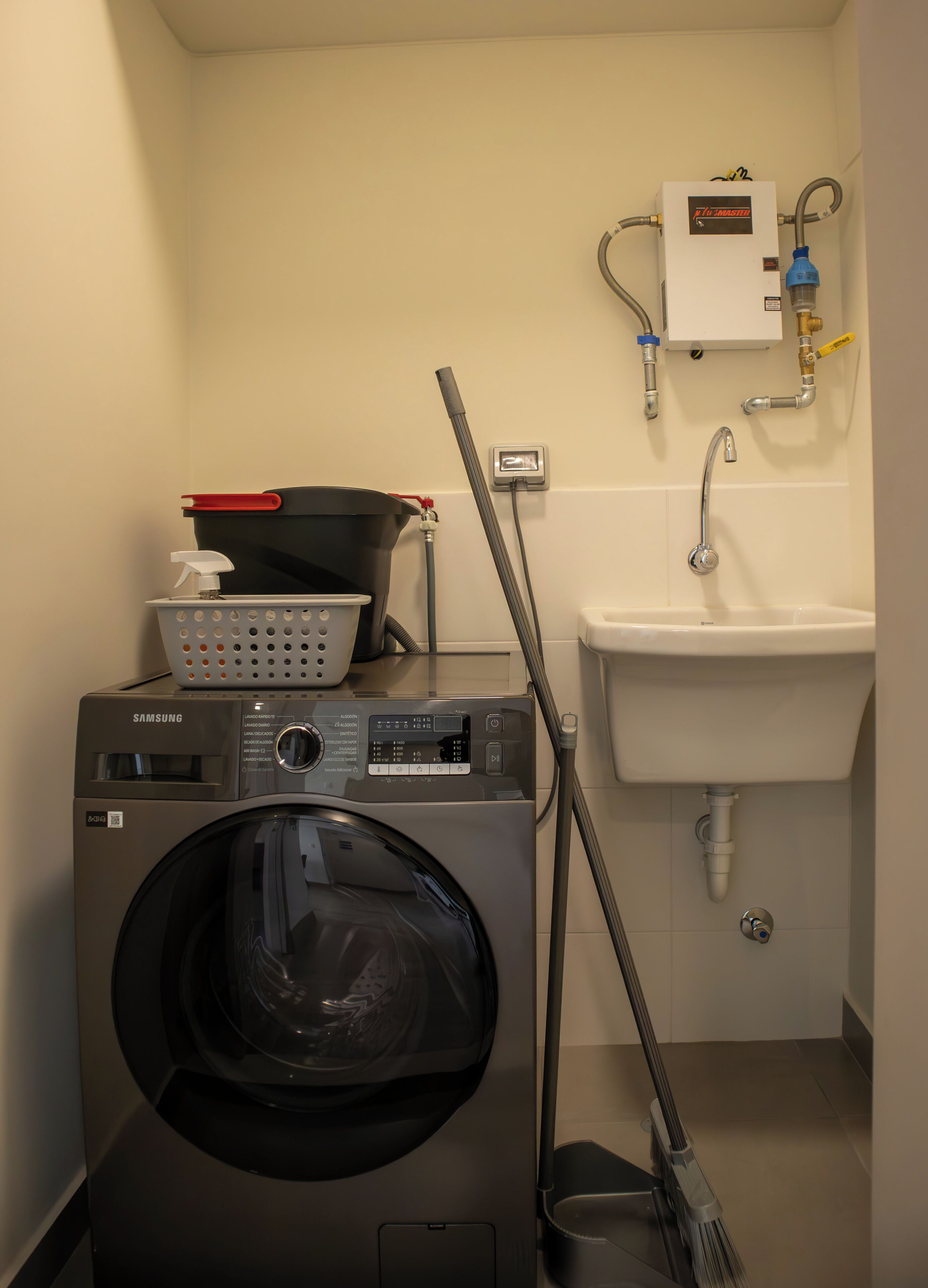 Een wasruimte met een Samsung wasmachine, een wasbak en een slang.