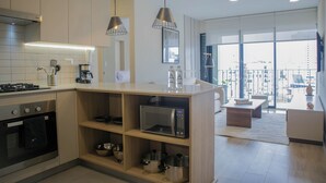 A modern kitchen with a built-in microwave, oven, and a coffee maker. There is a wooden island with shelves and a seating area in the dining space. - Pod by Wynwood House (Lima)