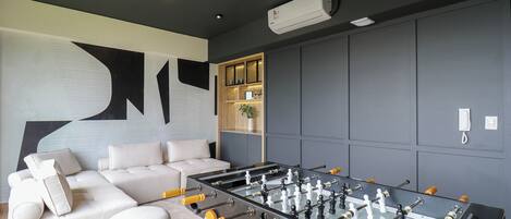 A modern living room with a foosball table, a sofa, and a wall-mounted cabinet.