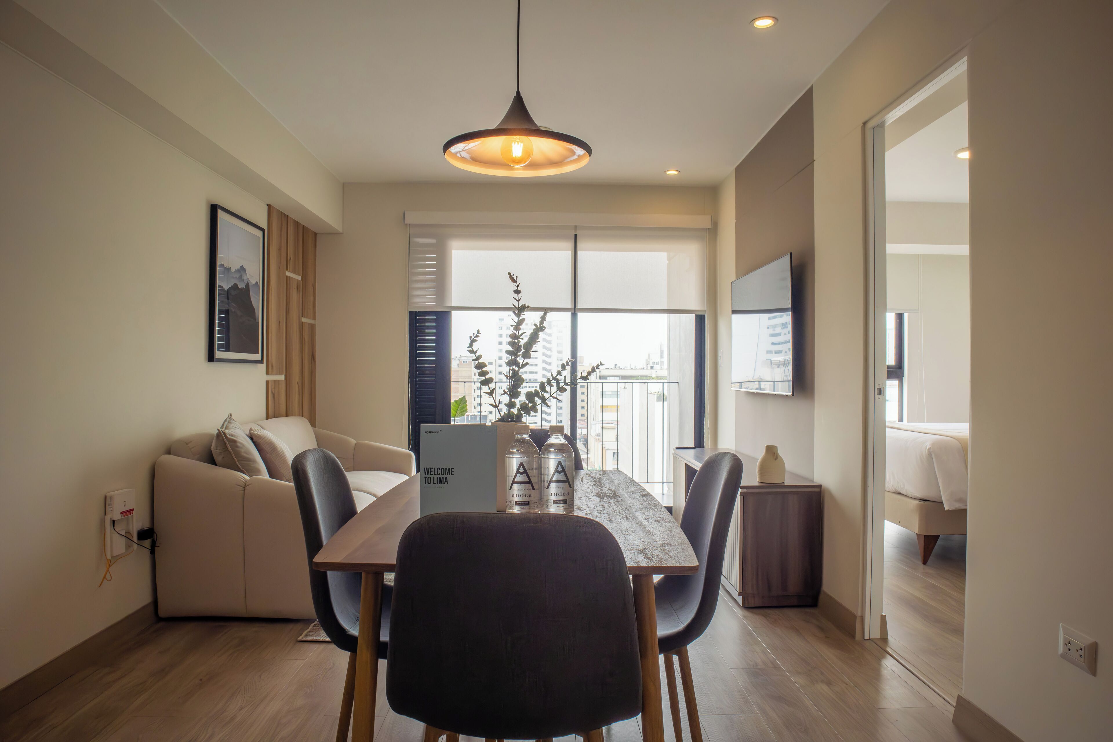 Un espacio de estar moderno con comedor, sofá, televisor y un balcón con vistas.