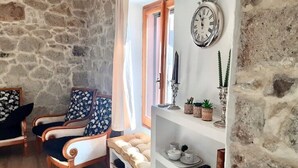 A cozy living room with a stone wall, two armchairs, a sofa, a bookshelf, and a wall-mounted clock. - Brand new house in Sardinia -ultrafast internet (Laerru)