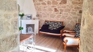 A stone-walled room with a sofa and two armchairs, a fireplace, and a dining area with a table and chairs. - Brand new house in Sardinia -ultrafast internet (Laerru)