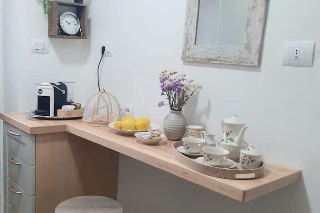 Una encimera de cocina con una cafetera, un florero con flores y un frutero.