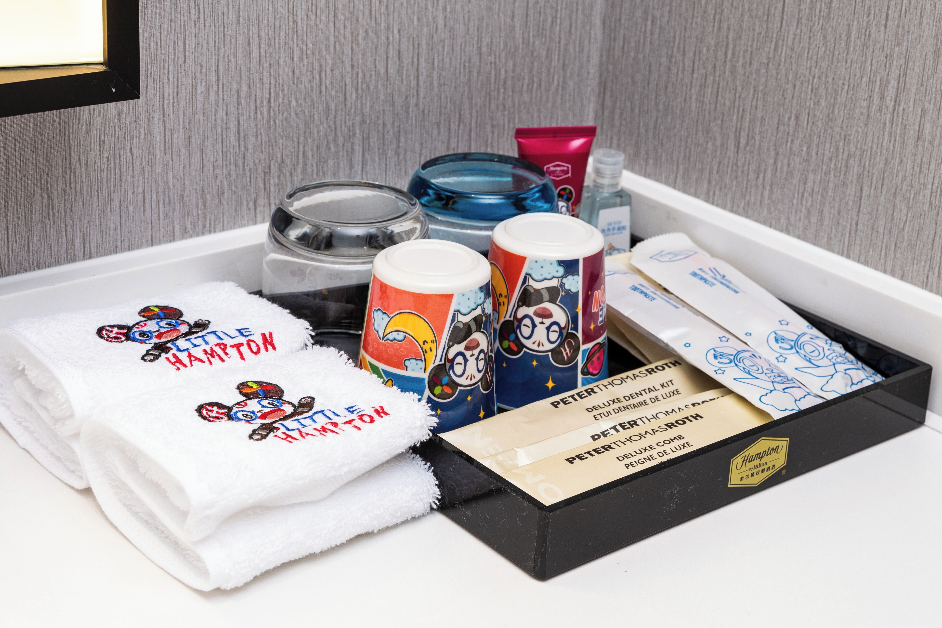 Habitación de hotel con un tocador ordenado, que incluye un toallero con toallas, un portacepillos de dientes, un dispensador de jabón y un cepillo de dientes.
