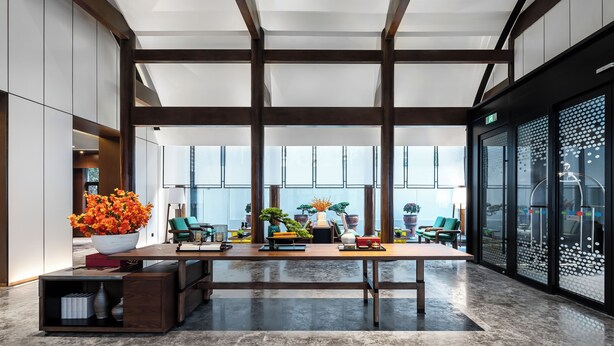 Eine geräumige Lobby mit hoher Decke, großen Fenstern und einem zentral platzierten Holztisch.