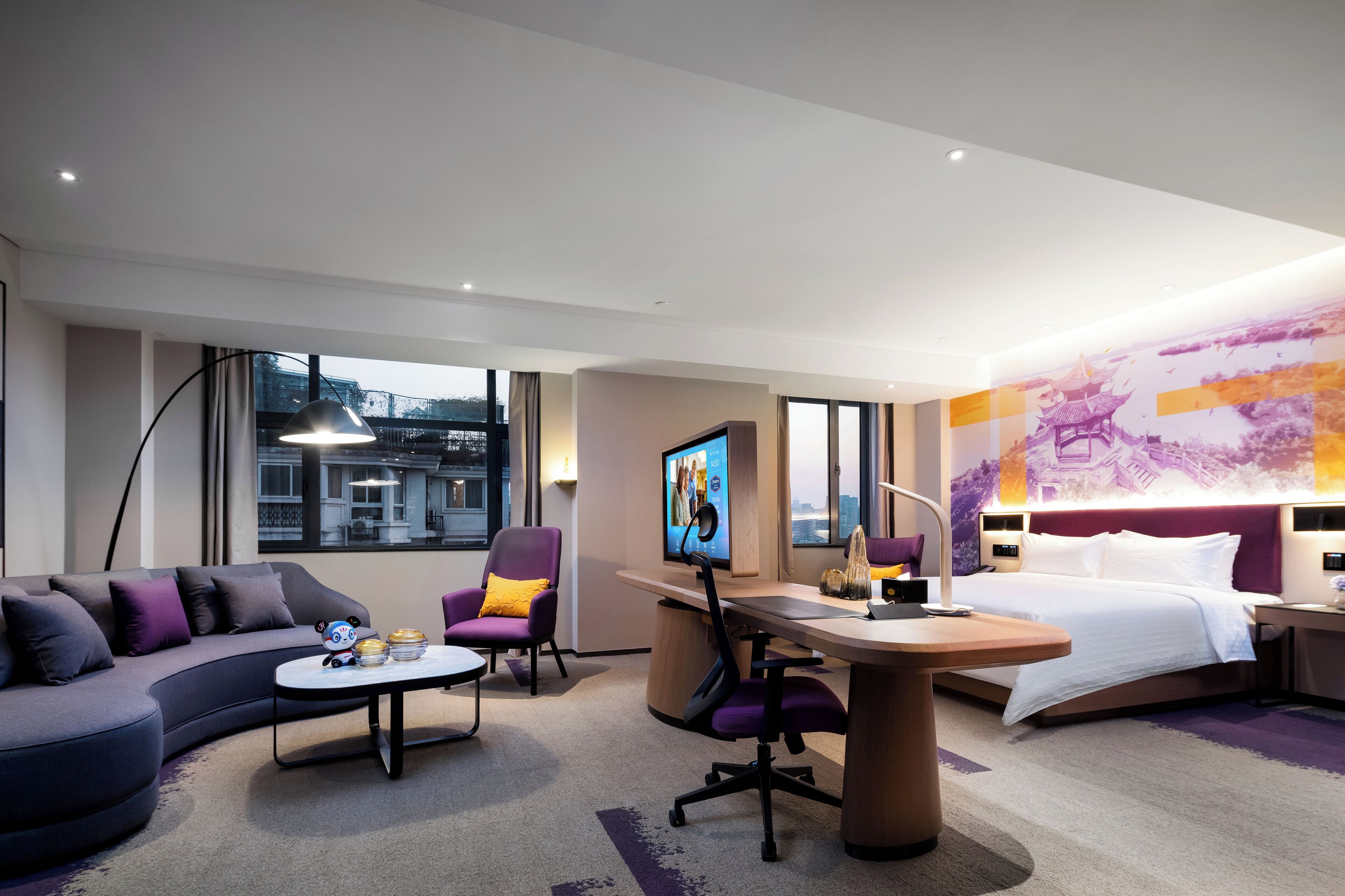 Habitació d'hotel moderna amb un sofà corbat, un escriptori, un llit i una finestra gran que ofereix vistes a la ciutat.
