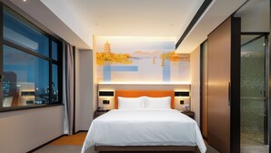 Ein modernes Hotelzimmer mit einem großen Bett, Blick auf die Stadt durch raumhohe Fenster und einer dekorativen Wandmalerei.