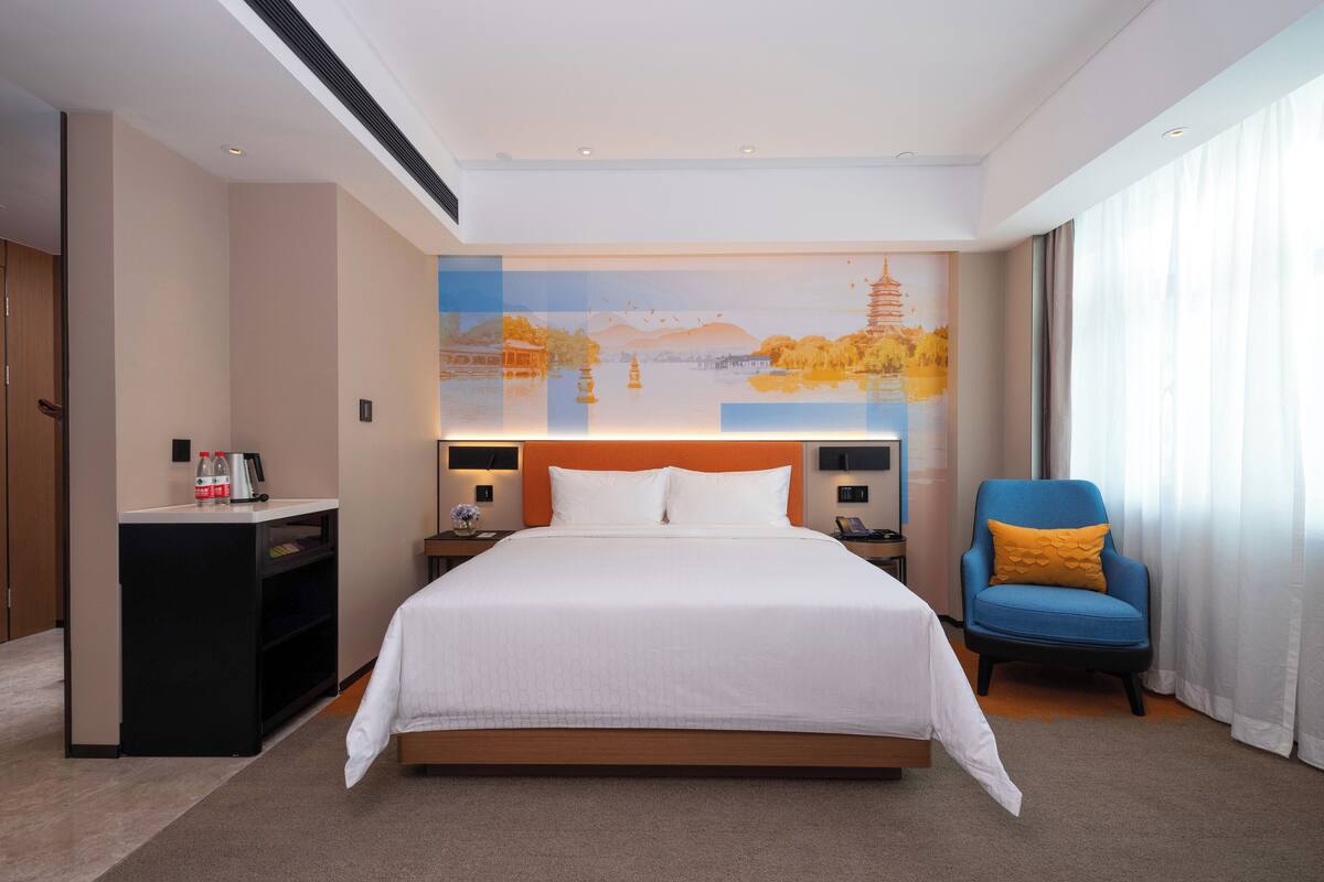 A hotel room with a large bed, a desk, a chair, and a painting on the wall.