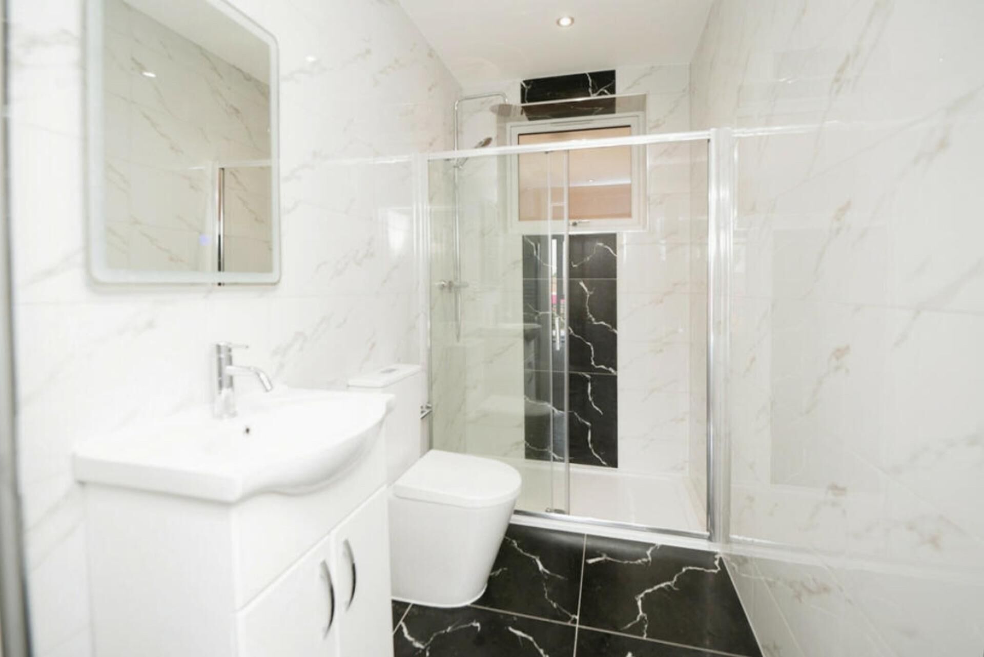 Une salle de bain avec un lavabo blanc, des toilettes et une douche fermée par des parois en verre.