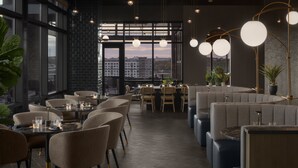 Een modern restaurant met ronde tafels, comfortabele zittingen, grote ramen met uitzicht op de stad en hanglampen.