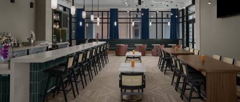 Un restaurante moderno con área de bar, techo alto con vigas a la vista y una variedad de opciones de asientos, incluyendo taburetes y mesas.