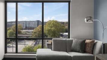 A modern hotel room with a large window offering a city view, a gray sofa, and a minimalist side table.