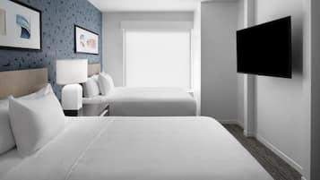 A hotel room with a large bed, a smaller bed, a TV mounted on the wall, a desk with a lamp, and artwork on the wall.