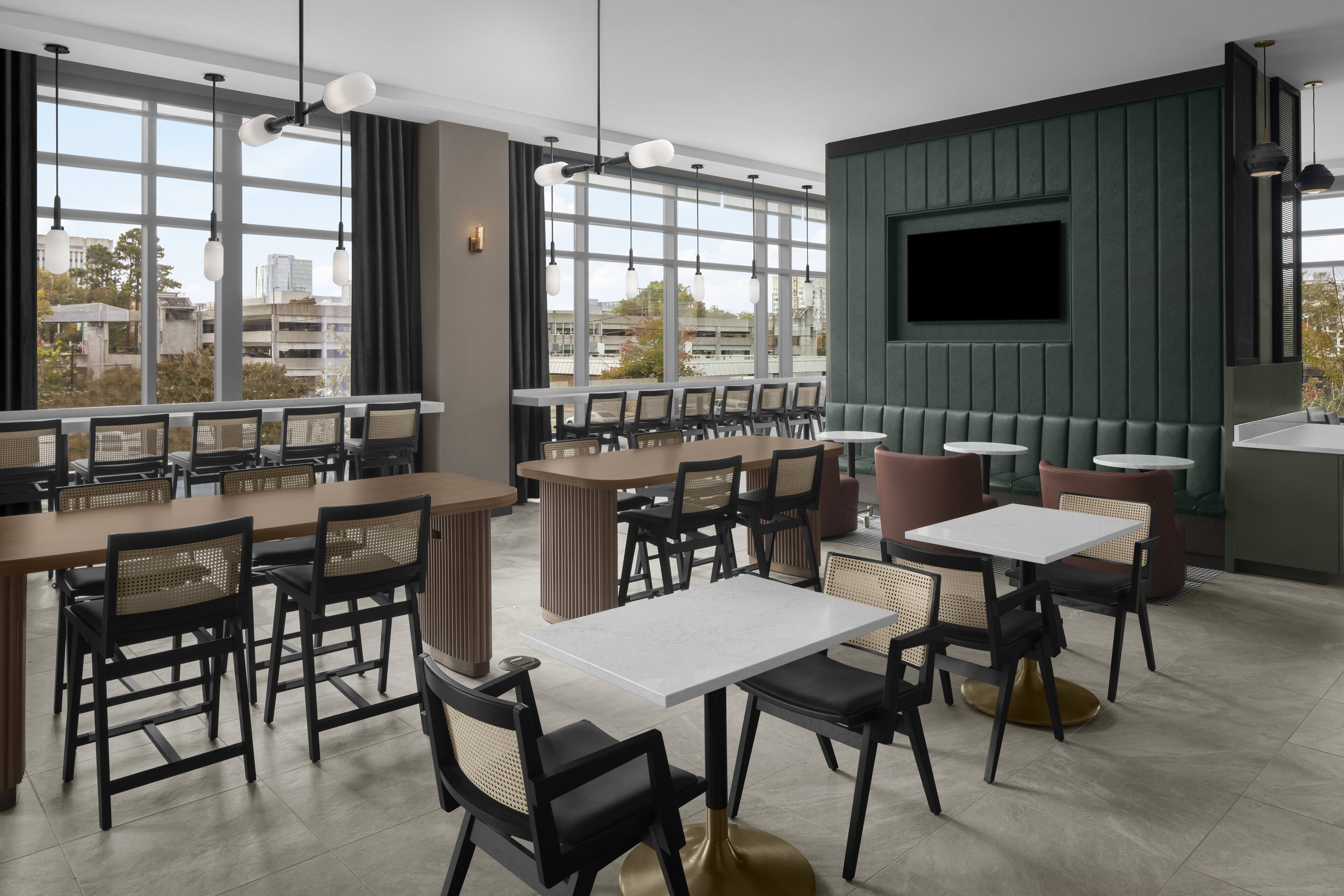 A modern restaurant with multiple dining tables and chairs, large windows, and a flat-screen TV mounted on the wall.