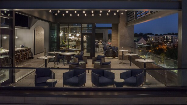 Een moderne rooftopbar met terras, een bar en een uitzicht op de stad in de schemering.